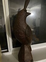 Front and side view of hand-carved wooden bird sculpture with detailed feather patterns and raised tail, mounted on wooden base.