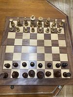 Top view of the wooden chessboard with all chess pieces arranged for the start of a chess game, showing alternating light and dark squares and chess pieces in two wood tones.