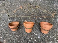 Wrought iron wall-mounted plant holder with three terracotta pots placed on ground, visible rust and weathering