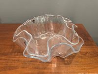 Single medium sized clear glass bowl with ruffled edge on wooden surface showing Muurla sticker