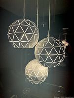 Front angled view of lit 3-light pendant with geometric triangular cutout globes hanging at different heights.