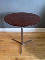 Front view showing circular wood tabletop and polished steel three-leg base