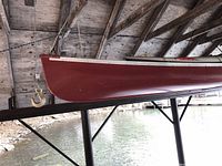 Front bow section of red fiberglass canoe hanging under shelter