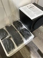 Subwoofer and five satellite speakers in original packaging with owner's manual placed on top of subwoofer.