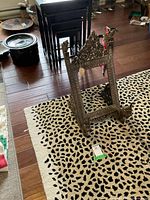 Full view of the ornate carved wooden holder placed on a leopard print carpet, showing its size relative to surrounding items.