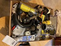 Photo from above showing a box filled with assorted boating parts including hoses, gauges, connectors, battery switch, and fuse holder.