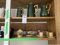 Wide view of assorted porcelain and ceramic cups, pitchers, teapot on shelves, showing collection variety and condition.