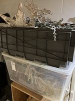 Stack of large plastic storage bins containing assorted wreaths and ornaments, some decorative stars visible on top.