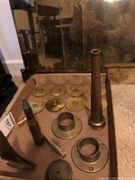 Multiple brass nautical parts laid out on cardboard including round numbered disks, bullet-shaped item, conical tube, and flanges.