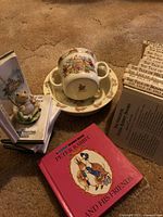 Adjacent view of the Beatrix Potter books collection and the Royal Doulton Bunnykins set consisting of baby cup, saucer, and small plate showing bunny motifs.