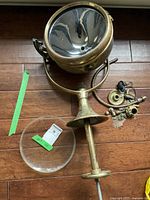 Brass ship's spotlight with glass front and assorted parts on a wooden floor.