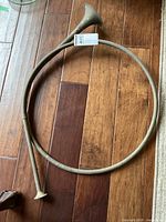 Full view of coiled brass bugle horn with natural patina and some dents, laying on wooden floor.