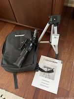 Photo of the telescope, tripod, carry bag, and instruction manual arranged on a wooden floor.