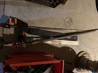 Large clamps with long metal bars and orange and black handle clamps lying on concrete floor