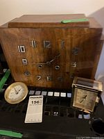 Photo showing the large wooden wall clock with metal numerals and two smaller clocks in front