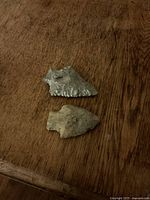 Two vintage stone arrowheads displayed on wooden surface with clear view of one broad triangular with serrations and one narrow pointed arrowhead.