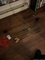 Full view of bow and four arrows laid on wood floor with bowstring partially coiled