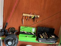 Image showing fishing rod, Invader reel, green and black tackle boxes with lures, and binoculars on shelf.