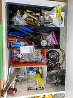 Drawer containing multiple plumbing tools and fittings including crimpers, pipe cutters, pressure gauges, and various brass fittings.