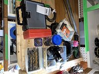 Photo of multiple tool sets including plastic storage cases with various drill bits, driver bits, and other small attachments laid out on a wooden table.