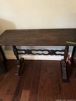 Front angle view of dark brown wooden console table showing carved legs and stretcher with minor surface wear
