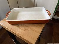 Top-side angled view showing full rectangular baking dish with orange exterior and white interior, placed on wooden table.