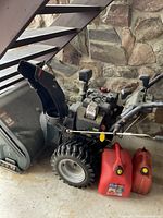 Side view of snowblower with large and small red gas cans beside it