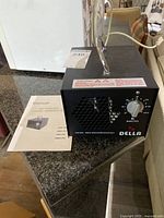 Black DELLA ozone generator with instruction manual on countertop.