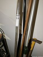 Side view of multiple yard tools including handles of broom, axe, shovel and others stored upright.
