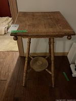 Front view of wooden Eastlake style fern table showing square top, turned legs, rounded finials, and circular lower shelf with concentric ring detailing.