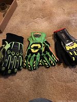 Three pairs of work gloves on beige carpet including one BDG pair with yellow and black pads, one green padded pair, and one black padded pair.