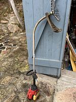 Full view of the gas-powered string trimmer with curved shaft and metal trimmer head attached, showing general wear and dirt.