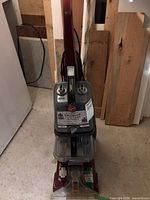 Front view of the Hoover corded electric carpet cleaner standing upright on a concrete floor with wood panels behind.