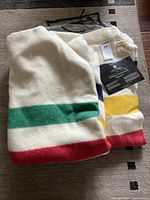 Folded cream wool blanket with multi-color stripes, plastic bag and MaxSold tag visible