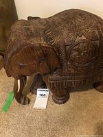 Side view of the wooden elephant carving showing carved details and ivory-like tusks.