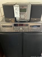 Full view of JVC sound system showing central unit, two bookshelf speakers on top, double cassette deck below, and two large floor speakers in front.