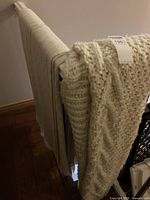 Three cream knitted blankets hanging over a drying rack: one bulky cable knit and two tighter knit style blankets.