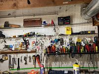 Wide view of wall-mounted pegboard with numerous hand tools including screwdrivers, wrenches, clamps, and measuring devices arranged on metal racks and hooks.