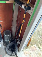 Fishing rods and net stored upright in corner, showing three rods and large net.