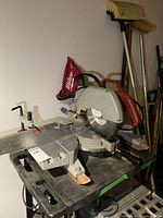 Full view of Milwaukee Magnum compound miter saw mounted on a black table with some adjacent cleaning tools in background