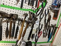 Photo of assorted hand tools hanging on pegboard including multiple hammers with wooden handles and various pliers and wrenches.