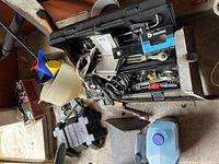 Wide view of open black hard plastic toolbox filled with assorted tools and workshop items including a plastic funnel and electrical cords.