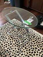 Full view of modern chrome side table with oval glass top on leopard print carpet.