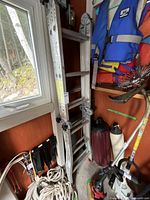 View of Featherlite ladder folded and stored leaning against a wall with ropes, trimmer, and life jackets nearby.