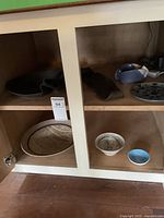Four pottery items inside a cabinet shelving: two bowls and two plates of varying colors and designs.