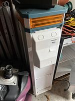 Front and angled views of the tall white rainproof power outlet with gray top and orange translucent panels, showing the Dockmaster logo and plug port covers.