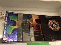 Overview of seven vinyl record albums standing upright showing spines and partial covers including Electric Light Orchestra and other albums.