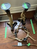 Photo showing pair of rustic medium antler candle holders and curved steel antler candle piece with three candle cups, arranged on floor.