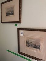 Two vintage framed prints hanging on wall showing maritime harbor scenes in ornate gold frames with mats.