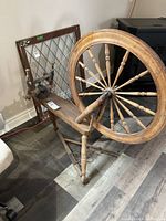 Front-side view of early wooden spinning wheel showing large wheel, foot pedal, and flyer mechanism